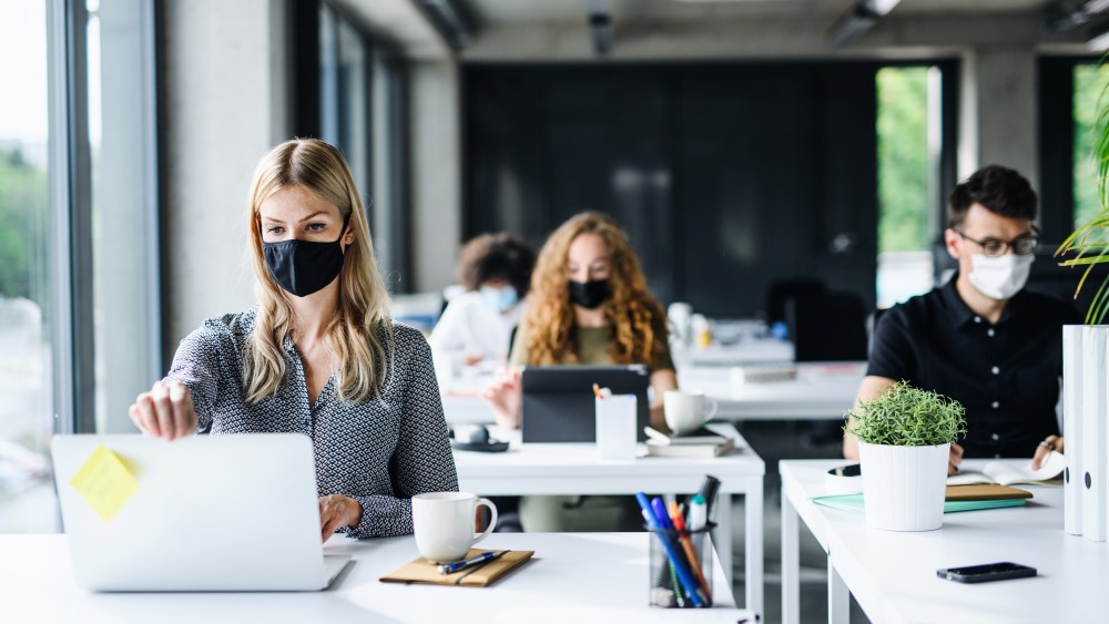 Young people with face masks back at work in office after coronavirus quarantine and lockdown.