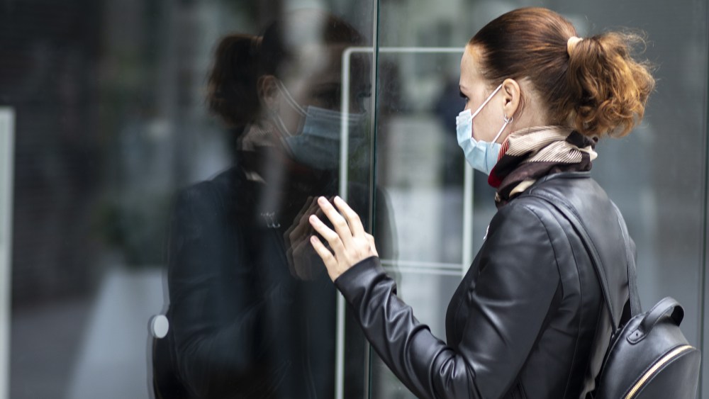 Sad woman at the entrance to a closed clothing store in a shopping center in a mask on her face. Closed store, shop because of Quarantine, coronavirus, covid-19
